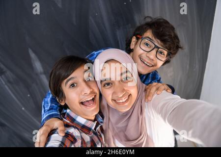 Gruppe von arabischen Teenagern, die Selfie-Fotos auf dem Smartphone mit schwarzer Tafel im Hintergrund machen. Selektiver Fokus Stockfoto