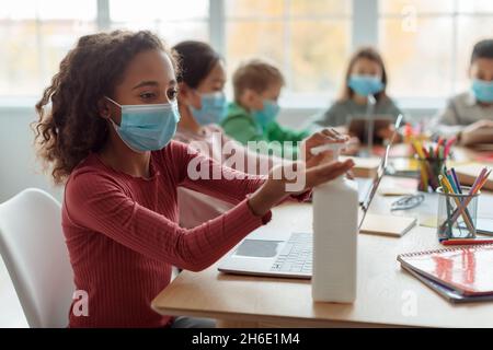 Schwarz Schulmädchen Desinfizieren Hände Tragen Gesichtsmaske In Der Schule Stockfoto