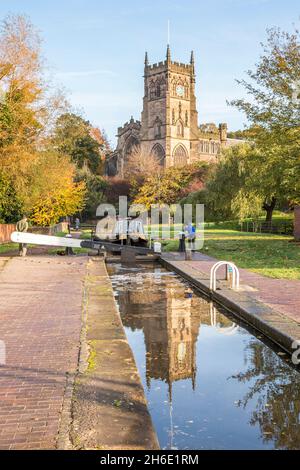 Kanalboot nähert sich im Sommer einer Schleuse mit einer Kirche im Hintergrund Stockfoto