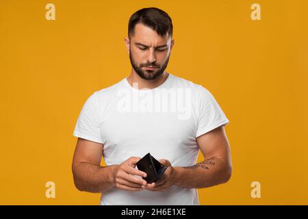 Enttäuschender trauriger europäischer Männerlook mittleren Alters bei leerer Brieftasche, isoliert auf gelbem Hintergrund Stockfoto