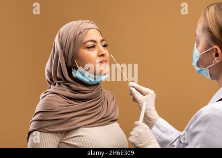 COVID-19 pcr-Testkonzept. Medizinisches Personal, das Nasenabstrich für Coronavirus-Probentest von infizierter muslimischer Frau nimmt Stockfoto
