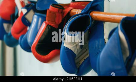 Mehrere Paar rote und blaue Boxhandschuhe, die auf einem Holzstab an einem hellen Wandhintergrund hängen Stockfoto