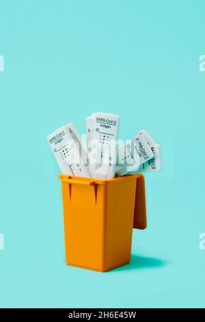 Nahaufnahme eines Mülleiters mit gebrauchten Covid-19-Antigendiagnosetestgeräten auf blauem Hintergrund, mit etwas Platz oben Stockfoto