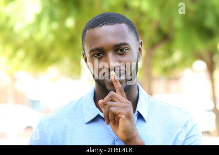 Glücklicher Mann mit schwarzer Haut, der mit Zeigefinger in einem Park um Stille bittet Stockfoto