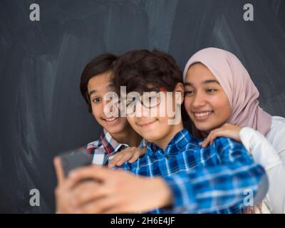 Gruppe arabischer Teenager, die Selfie-Fotos auf Smartphones mit schwarzer Tafel im Hintergrund machen Stockfoto