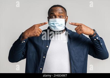 Afroamerikanischer Mann in medizinischer Maske zeigt die Finger darauf, empfiehlt sich vor Viruserkrankungen zu schützen, während einer Pandemie in Sicherheit zu bleiben, schwarzer Mann mit bedecktem Gesicht Stockfoto