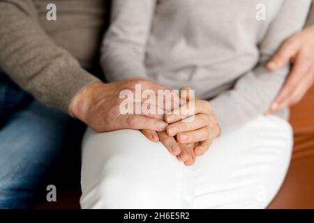 Nahaufnahme der Hände eines Ehepaares mittleren Alters, das die Hände zu Hause zusammenhält, Gesichter sind nicht sichtbar. Konzept der Unterstützung und Fürsorge in der Ehe Stockfoto