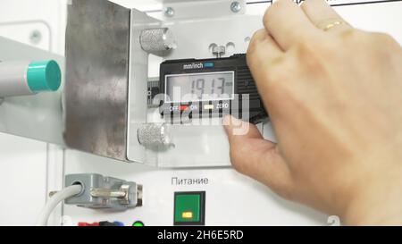 Elektronischer digitaler Bremssattel auf weißem Armaturenbrett. Industrieller Hintergrund mit einer männlichen Hand mit professionellem Werkzeugsattel, Messgenauigkeit. Stockfoto