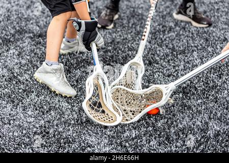 Blick auf einen Ball in der Netztasche eines Lacrosse Sticks, der von einem schwarzen Handschuh über einem Kunstrasen-Sportplatz gehalten wird. Stockfoto