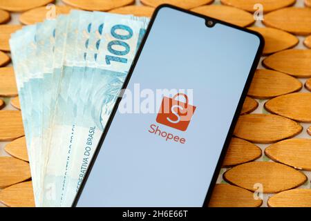 Minas Gerais, Brasilien - 19. April 2021: Smartphone-Handy-Bildschirm mit Shopee Marke und mehrere brasilianische echte Rechnungen Stockfoto