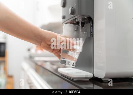 Nahaufnahme der Frau Trinkwasser wird aus dem Wasserkühler in die Glas-Trinkwassermaschine gegossen Stockfoto