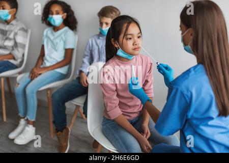 Krankenschwester macht PCR-Test für asiatische Mädchen, Testen von Kindern im Innen Stockfoto