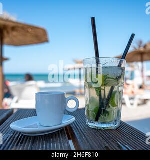 Kalter Mojito und Kaffee auf dem Tisch am sonnigen Strand Stockfoto