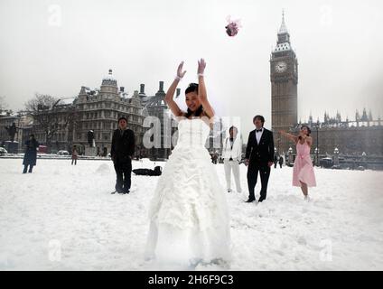 Eine neue chinesische Braut wirft ihren Blumenstrauß an ihre Hochzeitsgäste im Schnee auf dem Parliament Square in London. Stockfoto