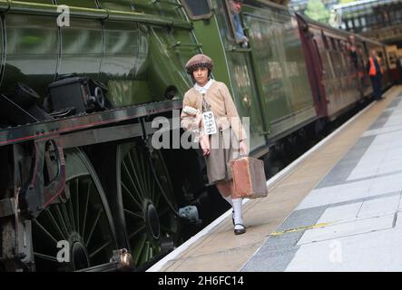 Ein Dampfzug, der die Reise von Hunderten von evakuierten Kindern nachstellt, die von einem Mann namens Oscar Schindler aus Großbritannien vor den Nazis gerettet wurden, kam heute am Bahnhof Liverpool Street in London an. Siebzig Jahre nachdem Sir Nichola Winton für 669 jüdische Kinder eine Reise von Prag nach London organisiert hatte, um den Konzentrationslagern zu entkommen, zogen einige der Überlebenden ihre Reise zurück. Sir Nichola, der im Mai seinen 100. Geburtstag feierte, war auf dem Bahnhof, um die Ankunft des Dampfzuges zu sehen. Ein junges Mädchen, das als Flüchtling aus dem Zweiten Weltkrieg gekleidet war, geht am Winton Train vorbei Stockfoto