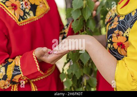 Kerl und Mädchen in hellen Nationalkostümen stehen sich gegenüber. Die Handfläche der Frau liegt auf der Handfläche des Mannes. Stockfoto