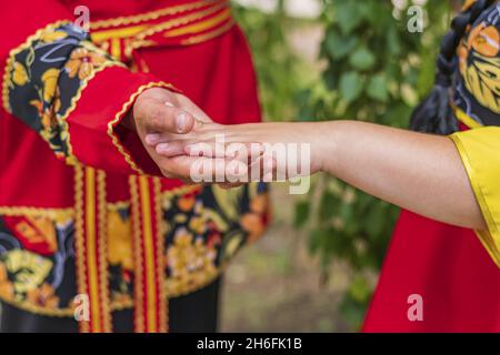 Kerl und Mädchen in hellen Nationalkostümen stehen sich gegenüber. Die Handfläche der Frau liegt auf der Handfläche des Mannes. Stockfoto