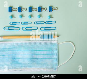 Komposition aus verschiedenen Schulmaterialien auf dem blauen Hintergrund und medizinischer Maske.Zurück zum Schulkonzept, Draufsicht. Stockfoto