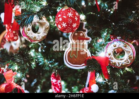 Weihnachtsschneemann, rote Kugeln, Handschuhe und Dekorationen hängen am Weihnachtsbaum. Festliche Einrichtung im Innenbereich. Neujahrsdetails und Atmosphäre Stockfoto