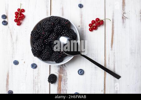 Frische Brombeeren auf einem Teller auf weißem Holzhintergrund. Stockfoto