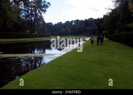 Menschen, die in den Studley Royal Water Gardens, Studley Royal Park, Fountains Abbey, Aldfield, in der Nähe von Ripon am Teich entlang spazieren, North Yorkshire, England Stockfoto
