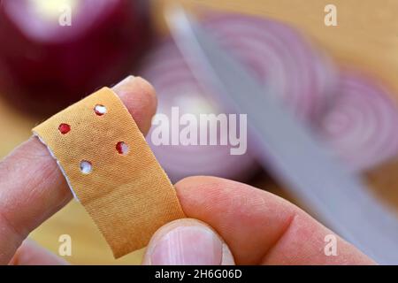 Nahaufnahme des Aufklemmers eines Bandes an einem Finger, der durch ein Messer verletzt wurde, während in der Küche Zwiebel geschnitten wurde Stockfoto