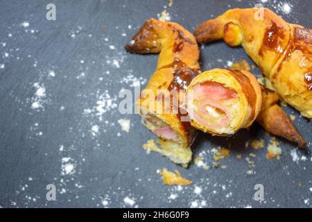 Frisch gebackene Croissants, gefüllt mit Schinken und geschmolzenem Käse, verzehrfertig, auf einem grauen Schieferteller Stockfoto
