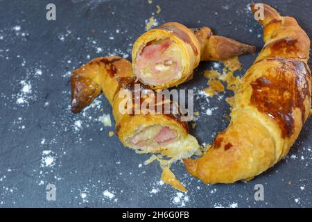 Frisch gebackene Croissants, gefüllt mit Schinken und geschmolzenem Käse, verzehrfertig, auf einem grauen Schieferteller Stockfoto