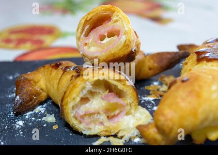 Frisch gebackene Croissants, gefüllt mit Schinken und geschmolzenem Käse, verzehrfertig, auf einem grauen Schieferteller Stockfoto