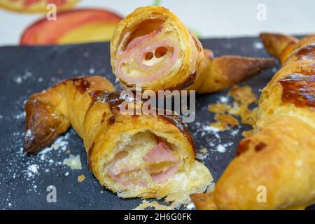 Frisch gebackene Croissants, gefüllt mit Schinken und geschmolzenem Käse, verzehrfertig, auf einem grauen Schieferteller Stockfoto