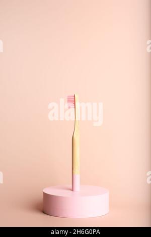 Eine umweltfreundliche Zahnbürste aus natürlichem Bambus auf einem runden Dekor auf einem rosa Hintergrund. Stockfoto
