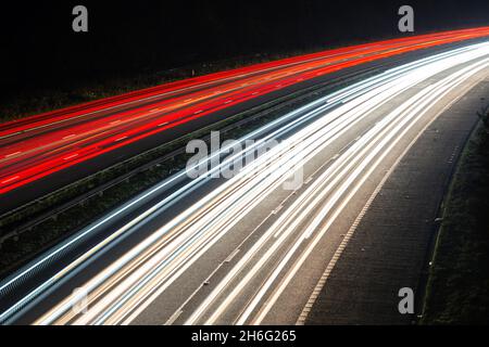 Nachts werden leichte Wege von einer verkehrsreichen Autobahn oder Autobahn angezeigt, die die Verkehrsbewegungen während der Hauptverkehrszeit zeigen. Der Verkehr scheint auf der linken Seite zu fahren Stockfoto