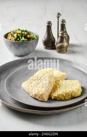 Halbfertiger Tintenfisch-Schnitzel in der Panade auf einem Teller Stockfoto