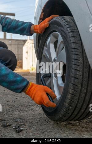 Autoreifen austauschen. Vertikales Foto des Fahrers mit Schraubenschlüssel beim Austausch des flachen Reifens Stockfoto