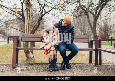 Liebevoller Ehemann unterstützt Frau Umarmung im Freien im Herbst Park. Traurige depressive Frau weint und bedeckt das Gesicht mit der Hand. Carering Mann hilft mit Schmerzen Stockfoto