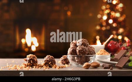 Vorbereiten von Schokoladenkugeln mit Mandeln als Süßigkeiten für Weihnachten auf Tisch mit dunklem Hintergrund mit Baum mit Lichtern und Kamin geschmückt. Vorderansicht Stockfoto