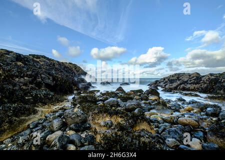 Eine Low-Angle-Ansicht von brechenden Wellen über die Felsen bei Penmon Point auf Anglesey, North Wales, Großbritannien Stockfoto