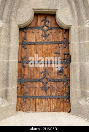 Gewölbte antike Kirche Holztür mit schwarzen Eisenornamenten in einer Steinwand. Stockfoto