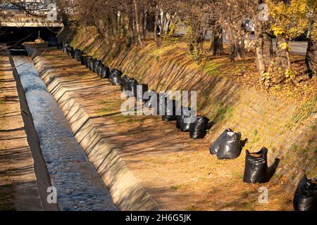 Gesackte Blätter in schwarzen Plastiktüten voller getrockneter Blätter, die an einem Flusskanal in der Innenstadt von Sofia, Bulgarien, Osteuropa, gesammelt werden können Stockfoto