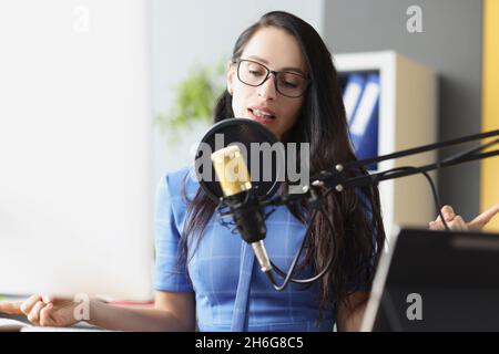 Junge schöne Frau spricht am Arbeitsplatz ins Mikrofon Stockfoto