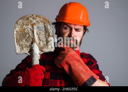 Baumeister in Arbeitshandschuhen und Hut mit Spaten. Männlicher Arbeiter im Helm mit Schaufel. Werkstatt oder Auftragnehmer Stockfoto