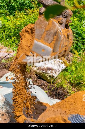 Der Straßenbagger gießt Sand aus und schafft so einen Fentry durch den Graben. Nahaufnahme auf dem Grashintergrund. Speicherplatz kopieren. Hochwertige Fotos Stockfoto