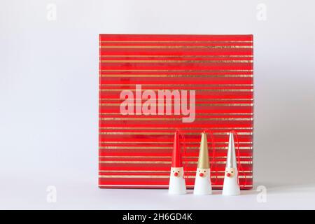 Drei Weihnachtsmänner-Figuren auf einer rot gestreiften Geschenkbox, weißer Hintergrund, Seitenansicht, Kopierbereich Stockfoto