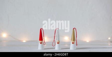 Drei Weihnachtsmänner-Figuren auf weißem Hintergrund, Girlande-Lichter, Seitenansicht, Kopierraum Stockfoto