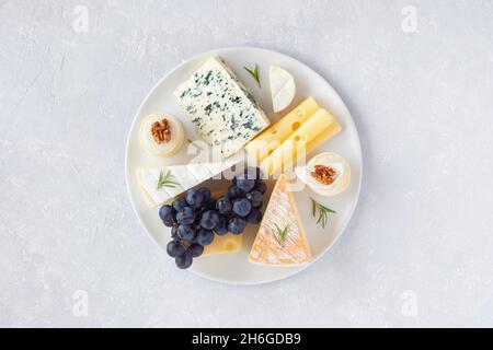 Käseplatte mit Trauben und Walnüssen auf grauem Betonboden, Draufsicht Stockfoto