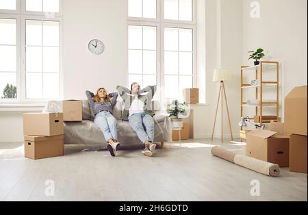 Zufriedenes junges Ehepaar, das sich entspannt und auf dem Sofa im neuen Zuhause sitzt. Stockfoto