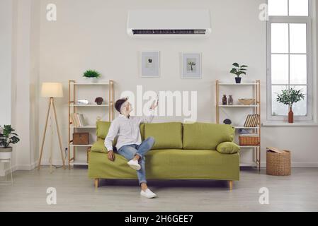 Der Mann, der die Klimaanlage wechselt, stellt eine angenehme Temperatur ein, während er zu Hause frische Luft genießt. Stockfoto