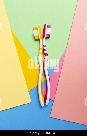 Vertikale Aufnahme von zwei rosa und gelben Zahnbürsten isoliert auf buntem Hintergrund. Stockfoto