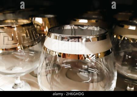Viele Klarglas-Becher. Herstellung von Glaswaren. Leere Gläser mit dekorativen Rändern im Werk. Verkauf von Geschirr im Laden. Stockfoto