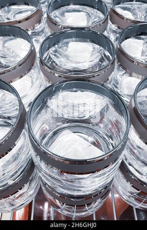 Viele Klarglas-Becher. Herstellung von Glaswaren. Leere Gläser mit dekorativen Rändern im Werk. Verkauf von Geschirr im Laden. Stockfoto